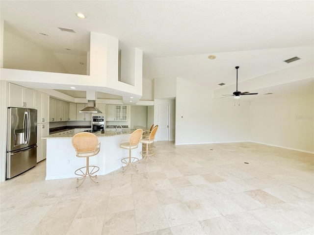 kitchen with high vaulted ceiling, a breakfast bar area, stainless steel fridge, a center island, and light stone counters