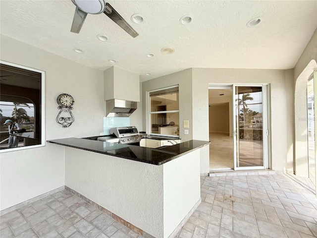 kitchen featuring range, a textured ceiling, kitchen peninsula, range hood, and white cabinets