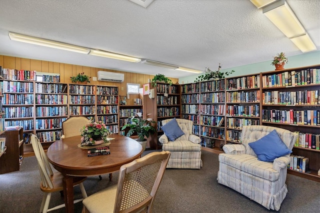 sitting room with dark colored carpet, an AC wall unit, a textured ceiling, and wood walls