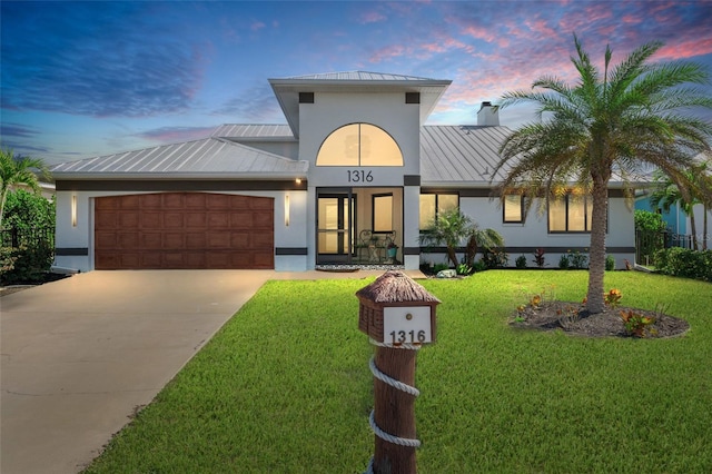 view of front of home featuring a garage, metal roof, a standing seam roof, a front lawn, and stucco siding