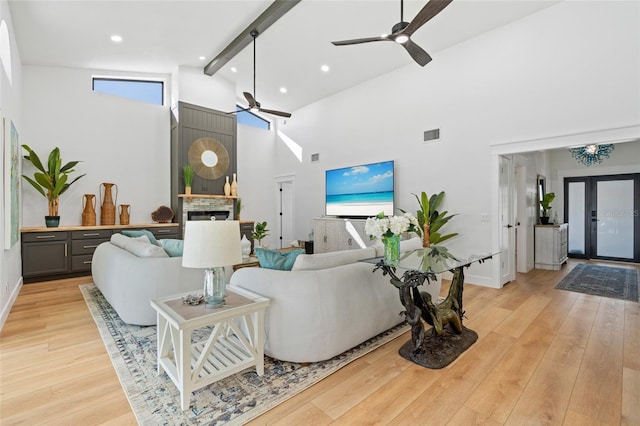 living area featuring light wood-type flooring, visible vents, beamed ceiling, and a stone fireplace