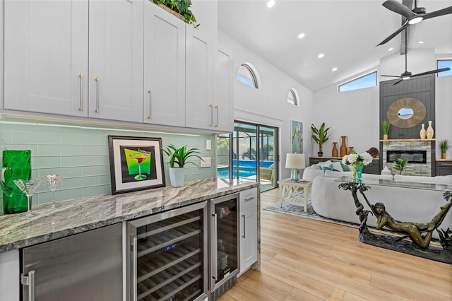 bar with ceiling fan, wine cooler, a fireplace, light wood finished floors, and tasteful backsplash