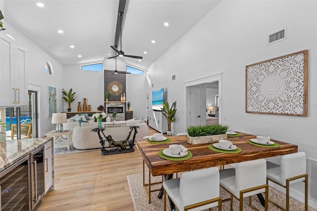 dining area featuring beverage cooler, visible vents, a ceiling fan, a glass covered fireplace, and light wood-style flooring