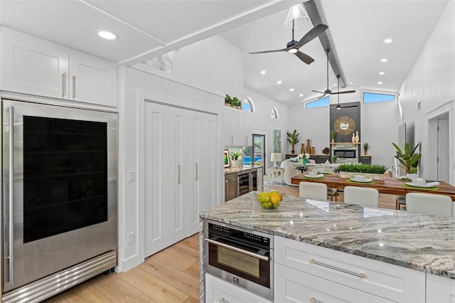 kitchen with light stone countertops, beverage cooler, white cabinetry, and oven