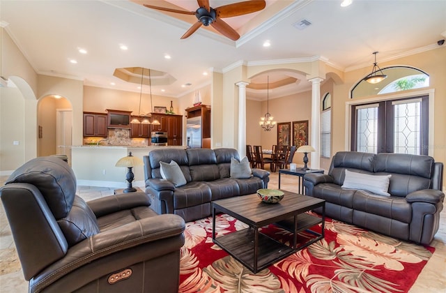 living room with ceiling fan with notable chandelier, ornamental molding, a tray ceiling, and decorative columns