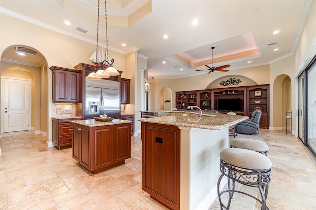 kitchen featuring stainless steel built in refrigerator, a kitchen bar, hanging light fixtures, a kitchen island with sink, and a tray ceiling