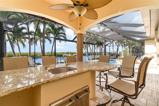 view of patio / terrace featuring a lanai, a wet bar, ceiling fan, and a water view