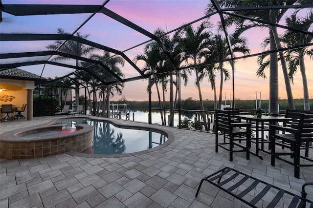 pool at dusk with an in ground hot tub, a water view, a patio, and a lanai