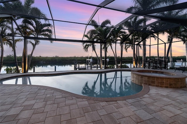 pool at dusk featuring an in ground hot tub, a water view, a patio, and a lanai