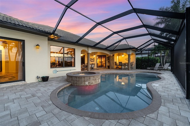 pool at dusk with an in ground hot tub, a lanai, and a patio