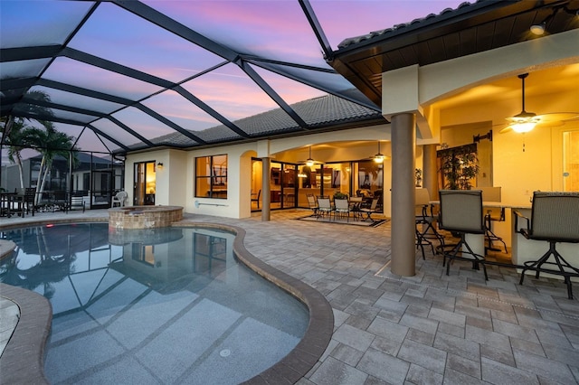 pool at dusk featuring a lanai, a patio, ceiling fan, and an in ground hot tub