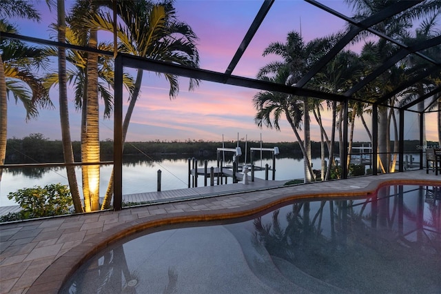 pool at dusk featuring a water view, a boat dock, and glass enclosure