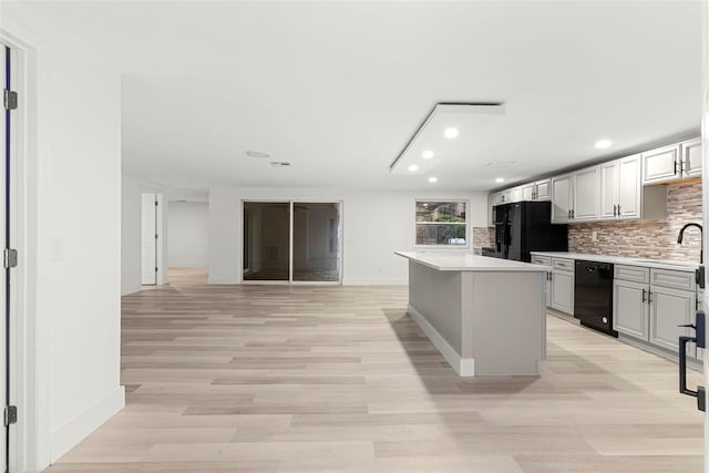 kitchen featuring white cabinetry, backsplash, a center island, black appliances, and light wood-type flooring