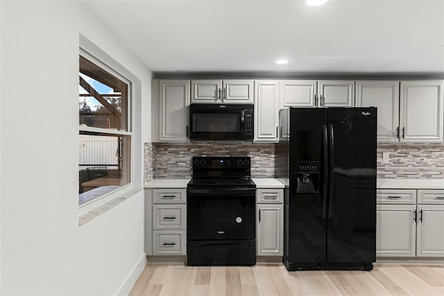 kitchen featuring backsplash, gray cabinetry, light hardwood / wood-style flooring, and black appliances