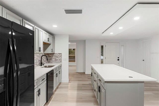 kitchen featuring sink, tasteful backsplash, black appliances, a kitchen island, and light wood-type flooring