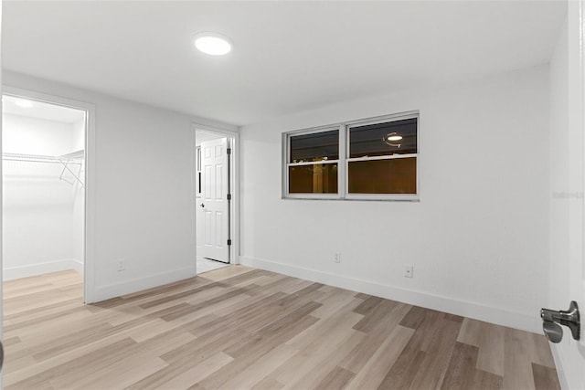 unfurnished bedroom with a walk in closet, a closet, and light wood-type flooring