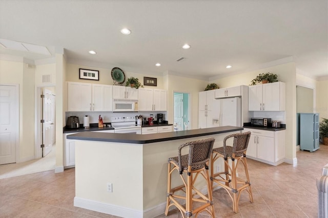 kitchen featuring a kitchen bar, a center island, white cabinets, and white appliances