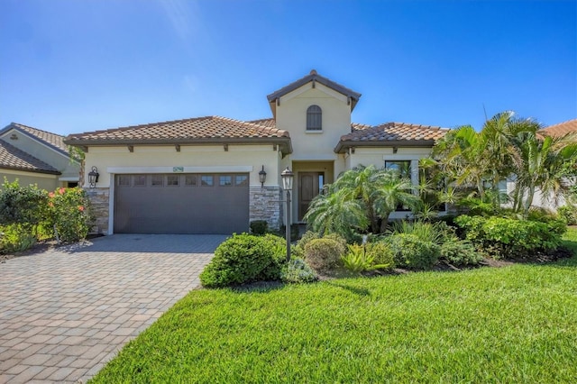 mediterranean / spanish-style house with stone siding, an attached garage, decorative driveway, a front yard, and stucco siding