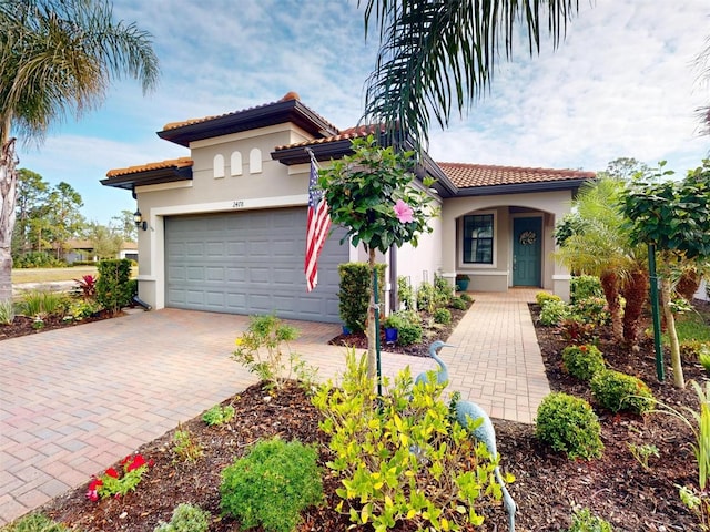 mediterranean / spanish home featuring a garage, a tile roof, decorative driveway, and stucco siding