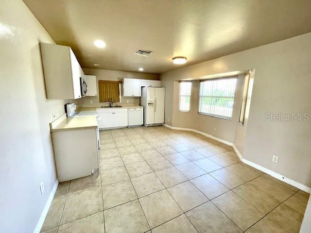 kitchen featuring white refrigerator with ice dispenser, sink, light tile patterned floors, and white cabinets