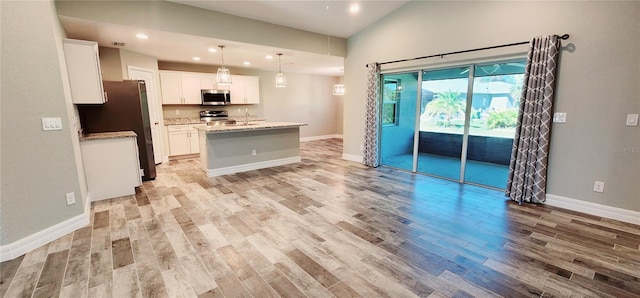 kitchen featuring white cabinets, an island with sink, hanging light fixtures, light stone countertops, and stainless steel appliances