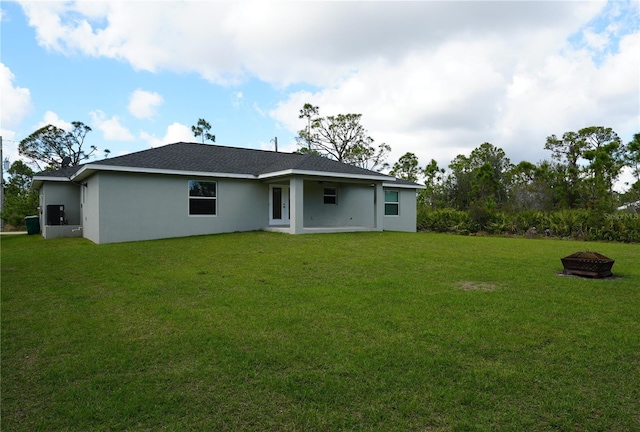 back of house with an outdoor fire pit, a lawn, and stucco siding