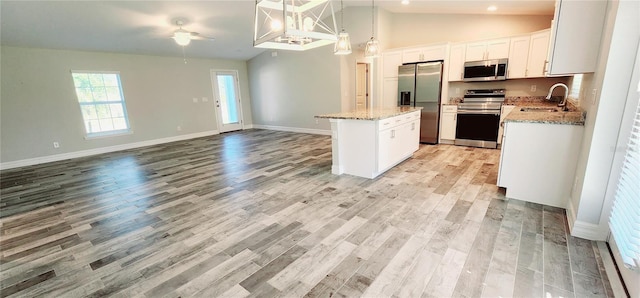 kitchen featuring appliances with stainless steel finishes, open floor plan, a center island, white cabinetry, and a sink