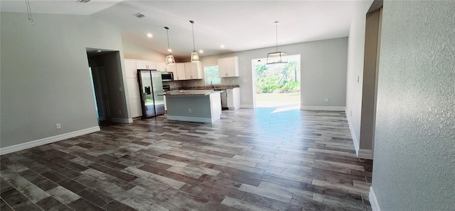 kitchen featuring white cabinets, dark countertops, a kitchen island, appliances with stainless steel finishes, and hanging light fixtures