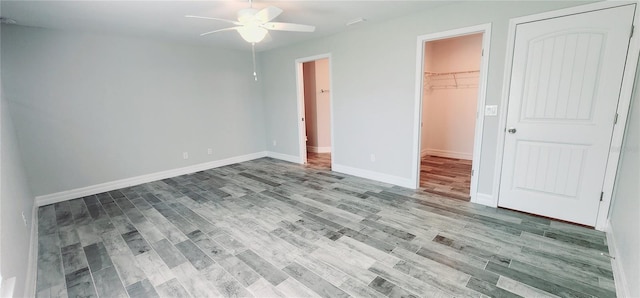 unfurnished bedroom with a walk in closet, a closet, a ceiling fan, wood finished floors, and baseboards