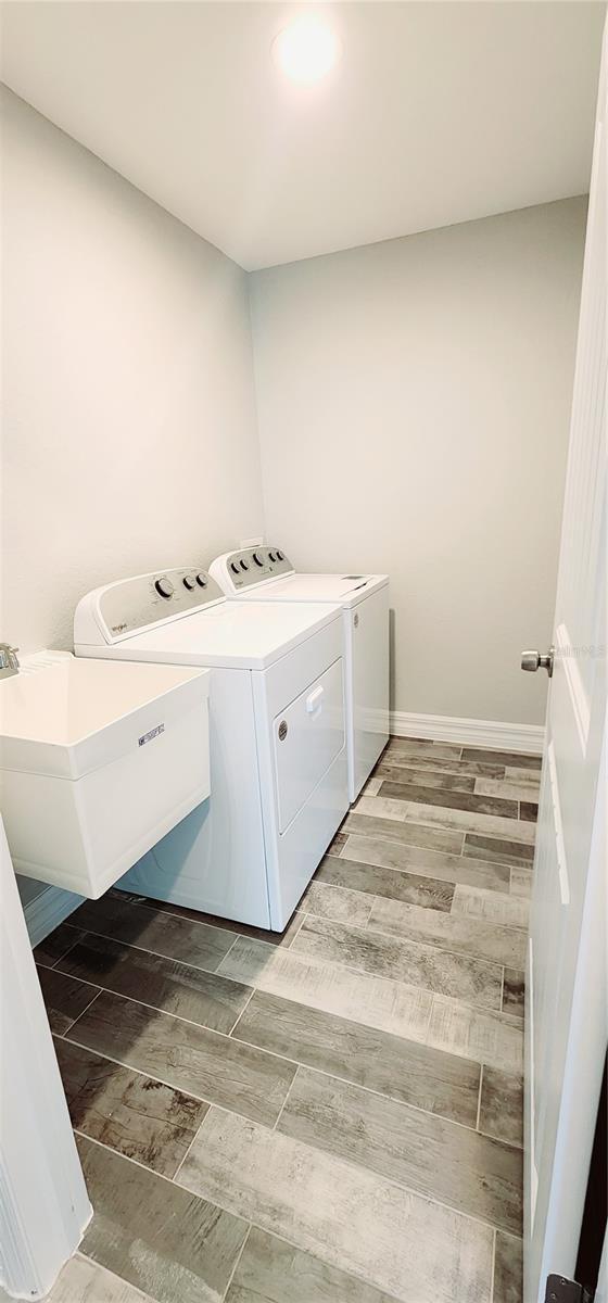 washroom with laundry area, a sink, baseboards, wood tiled floor, and washer and clothes dryer