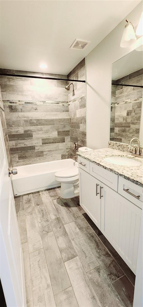 full bathroom with toilet, vanity, visible vents,  shower combination, and wood tiled floor