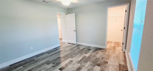 unfurnished bedroom featuring a walk in closet, wood finished floors, visible vents, and baseboards