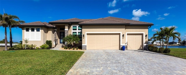 prairie-style house with an attached garage, stucco siding, decorative driveway, and a front yard