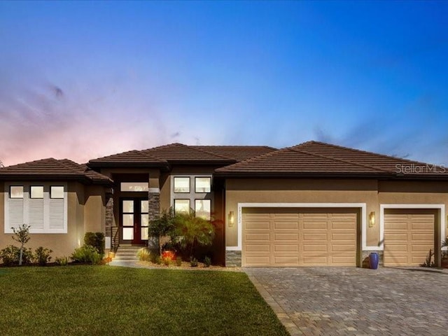 prairie-style home featuring a garage, stucco siding, decorative driveway, and a yard