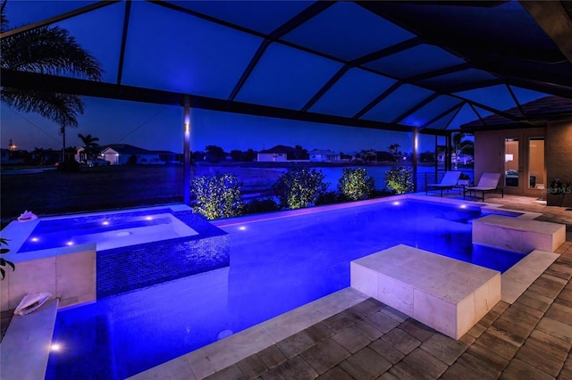 pool at twilight with french doors, a patio area, a lanai, and a pool with connected hot tub