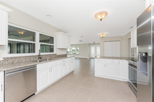 kitchen with sink, white cabinets, kitchen peninsula, stainless steel appliances, and light stone countertops