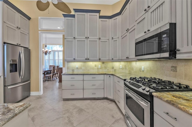 kitchen with stainless steel appliances, light stone countertops, light tile patterned flooring, backsplash, and ceiling fan with notable chandelier