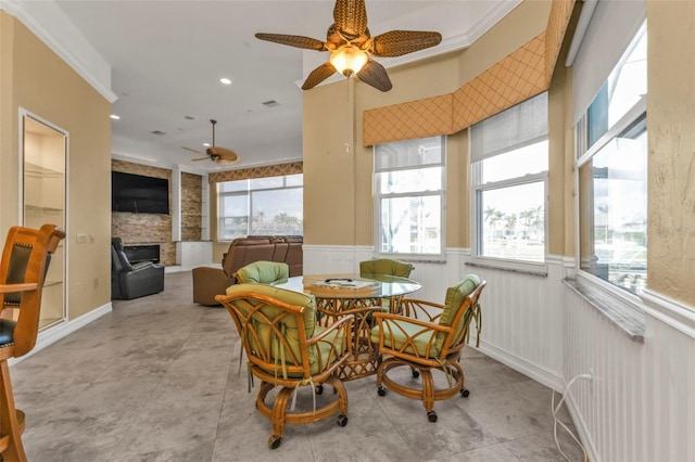 dining space featuring ceiling fan, a stone fireplace, and ornamental molding