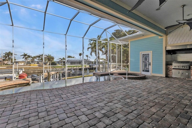 view of patio featuring grilling area, a water view, an in ground hot tub, glass enclosure, and an outdoor kitchen