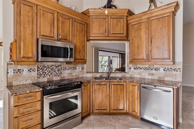 kitchen with sink, light tile patterned floors, appliances with stainless steel finishes, dark stone counters, and backsplash