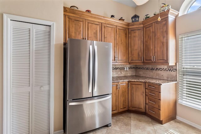 kitchen featuring stainless steel fridge, light tile patterned floors, decorative backsplash, and stone counters