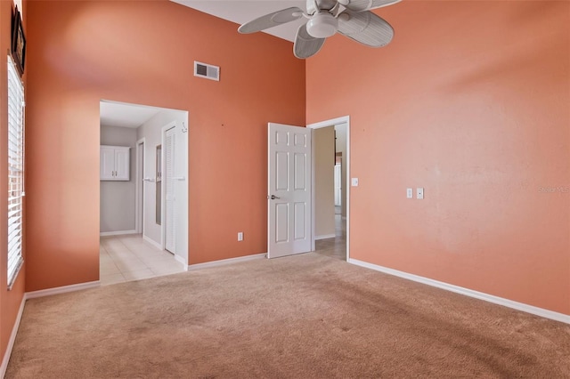 unfurnished bedroom featuring a high ceiling, light colored carpet, ceiling fan, and a closet