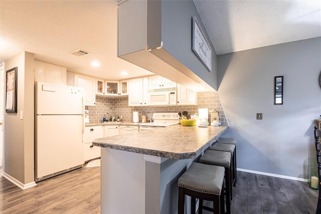 kitchen with a kitchen bar, sink, white cabinetry, kitchen peninsula, and white appliances