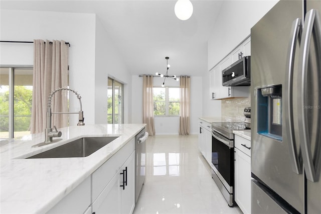 kitchen featuring light stone counters, hanging light fixtures, appliances with stainless steel finishes, white cabinetry, and a sink