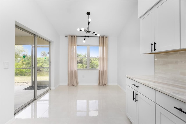 kitchen with a chandelier, white cabinets, hanging light fixtures, backsplash, and light stone countertops