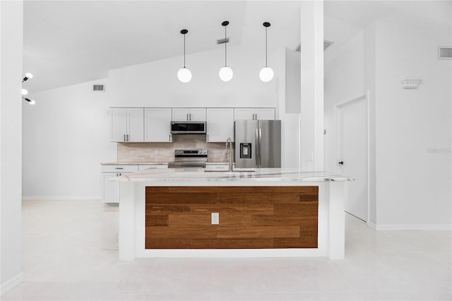 kitchen with light stone counters, stainless steel appliances, white cabinets, an island with sink, and decorative light fixtures