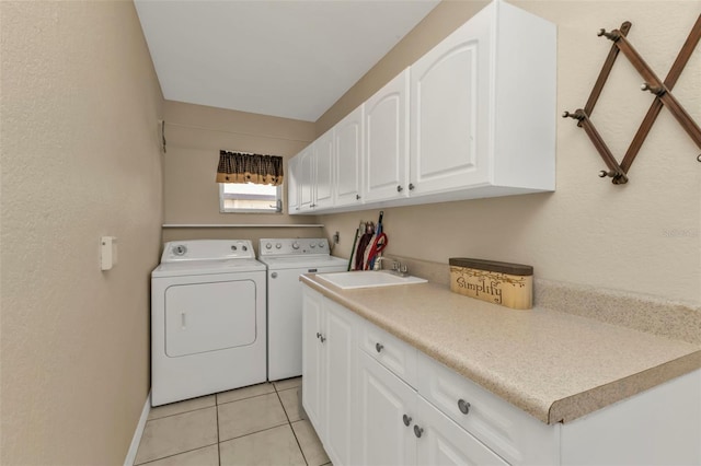 clothes washing area with light tile patterned floors, sink, washing machine and dryer, and cabinets