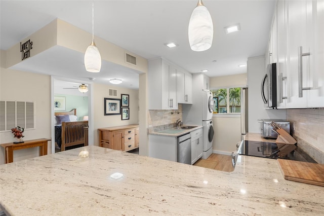 kitchen with white cabinetry, stacked washer / drying machine, kitchen peninsula, and pendant lighting