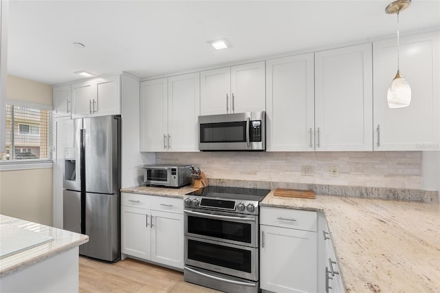 kitchen featuring stainless steel appliances, light stone countertops, hanging light fixtures, and white cabinets