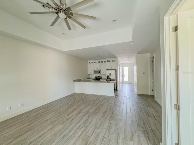 unfurnished living room with a raised ceiling, ceiling fan, and light wood-type flooring